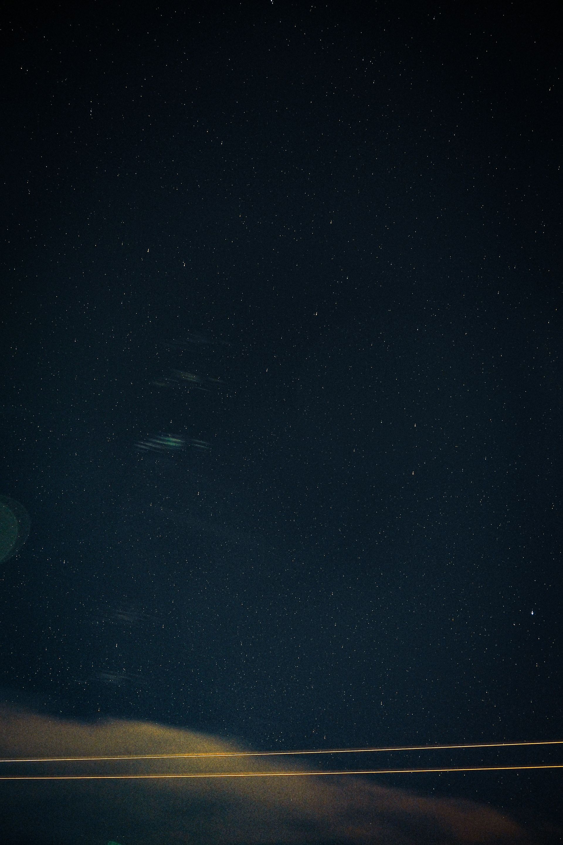 Um céu noturno cheio de estrelas, com nuvens baixas iluminadas e dois fios de luz atravessando a base